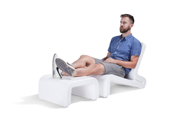 Image of a man sitting on a Line Lounge Chair, with his feet on a Line Ottoman made from resin. Great for indoor or outdoor.