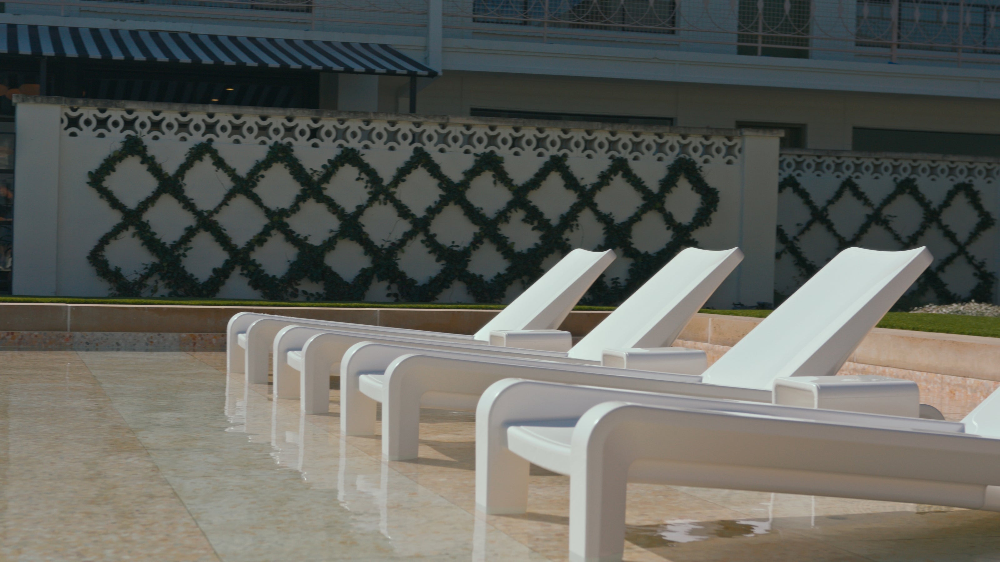 Row of white lounge chairs by a poolside with decorative wall in the background