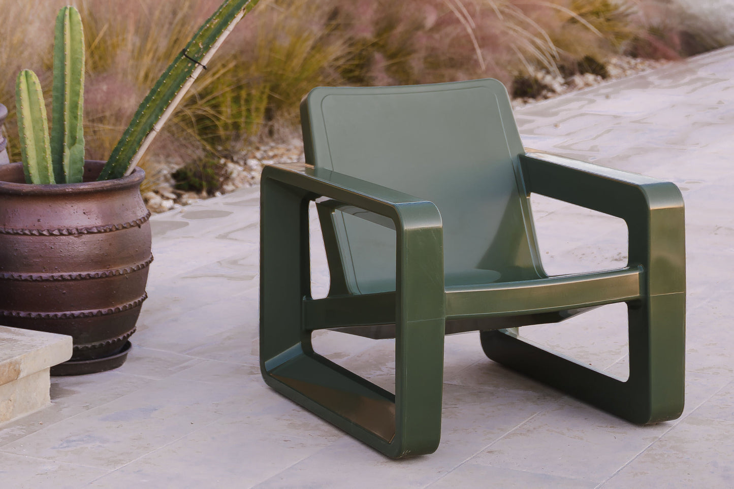 Green chair on a patio with a wooden pergola and pond in the background