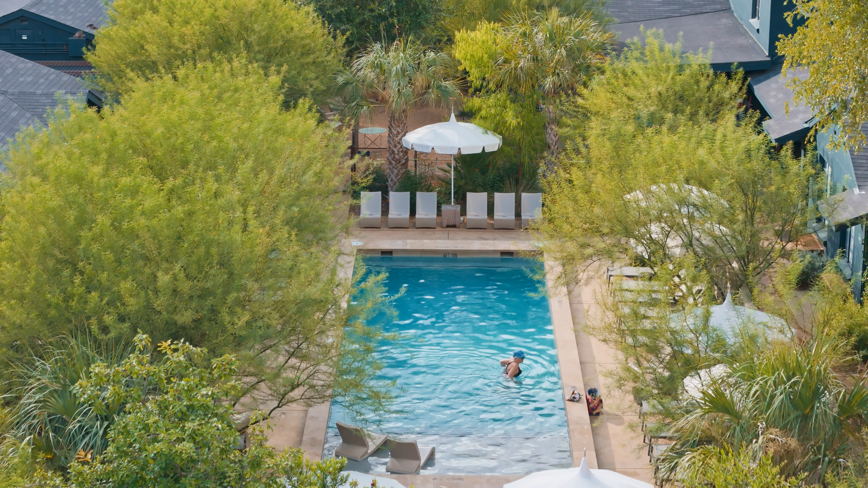 Pool area with lounge chairs, umbrella, and people in a garden setting