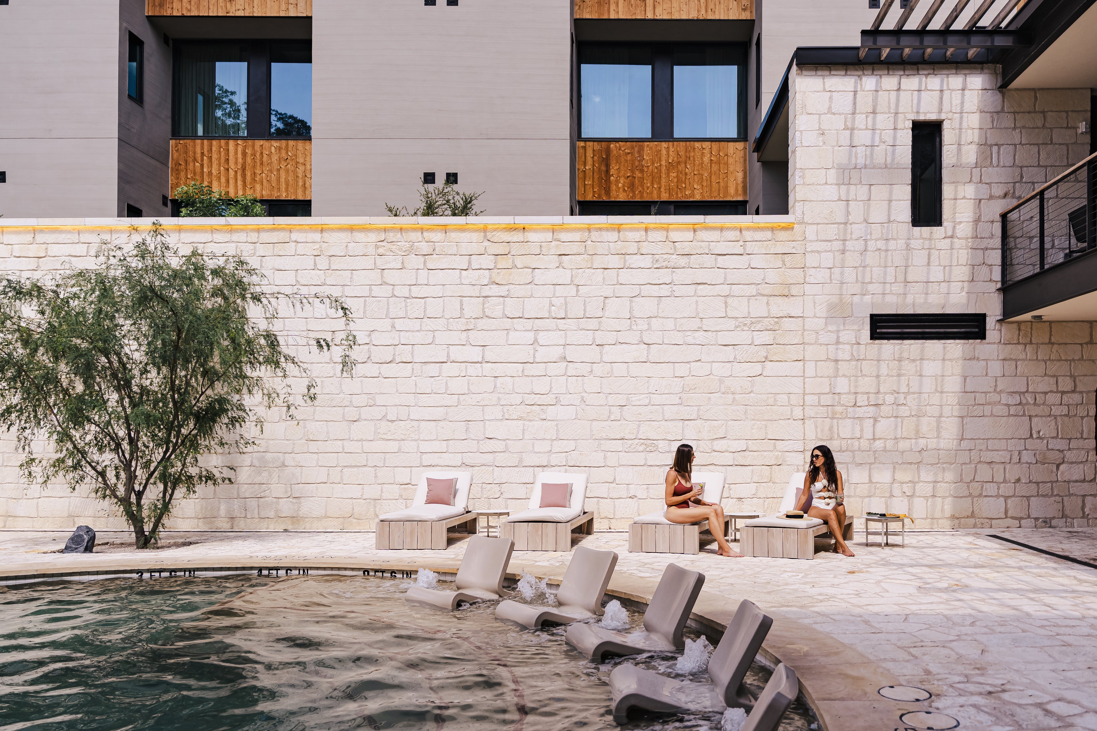 Two women sitting by a poolside with modern architectural background