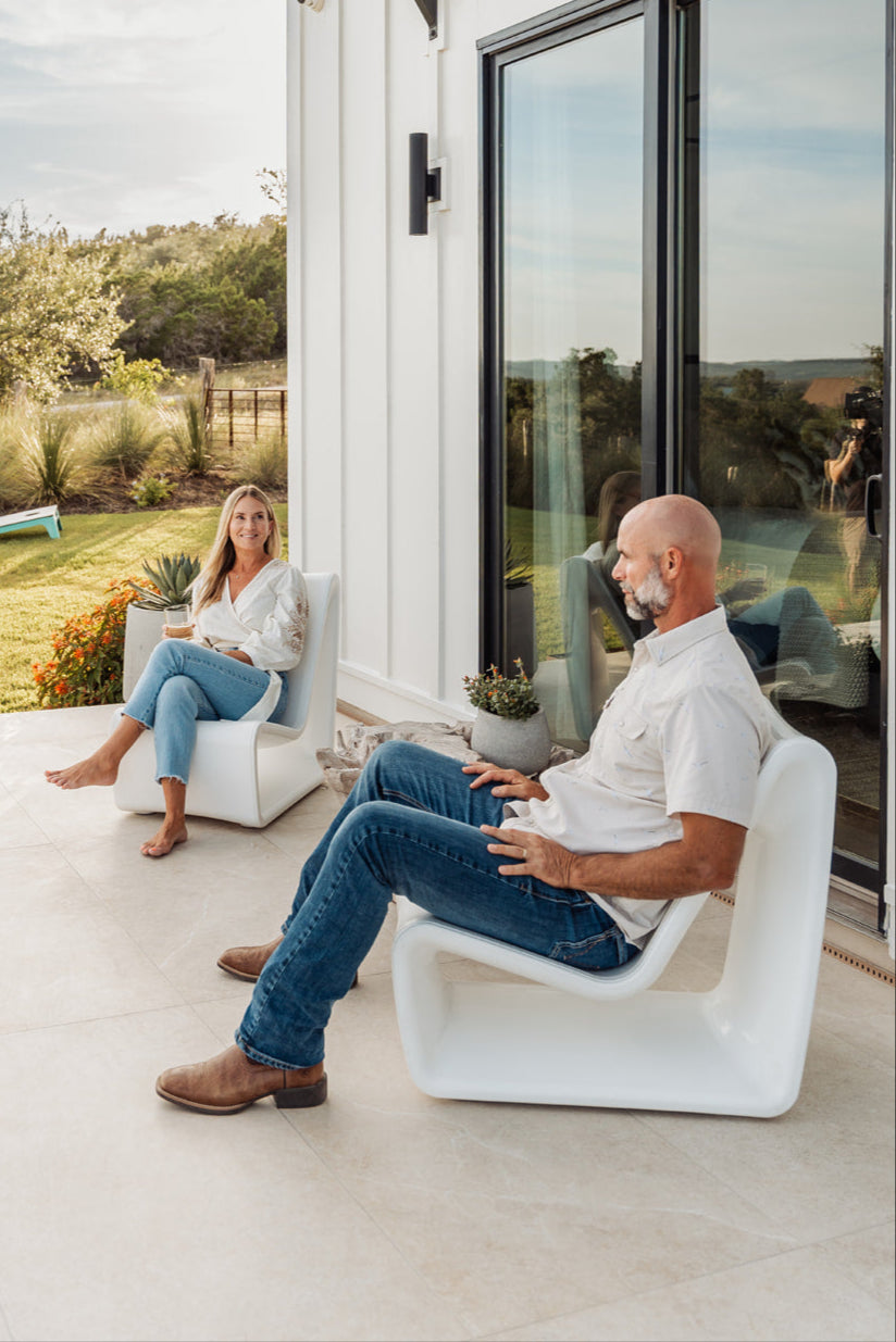 Two people sitting on modern outdoor chairs in front of a house.