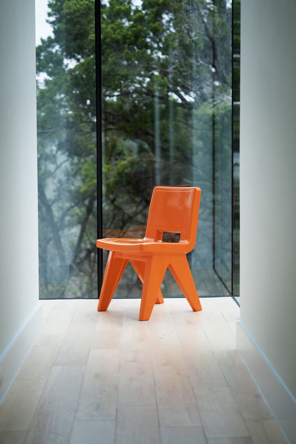 Image of an angled Fresco Dining chair made of resin in the colour Vintage Orange, displayed indoors, in front of a window.