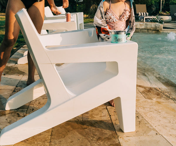 A side image of the modern, waterproof Bask Lounge Chairs in Highcloud White made with polyethylene, facing an outdoor pool. 
