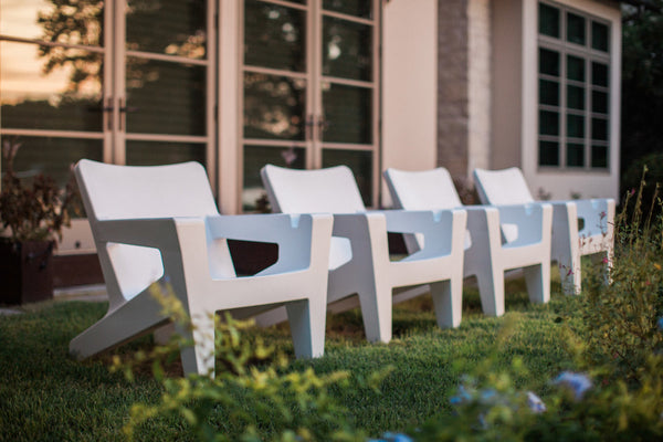 Image of a row of 4 all-weather Bask Chairs in Highcloud White outdoors on turf, inspired by the classic Adirondack style. 
