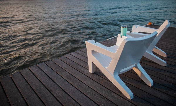 Image of 2 sleek, waterproof Highcloud White Bask Lounge Chairs made with polyethylene, displayed outdoors on a seaside deck.