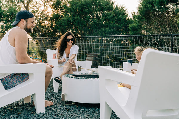 Image of the Bask Lounge Chairs in the color Highcloud White around an outdoor fire pit. Made of ultra-durable polyethylene. 