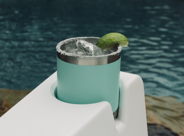 Close-up image of the cup holder on the arm of the Bask Lounge Chair in the color Highcloud White, facing an outdoor pool.