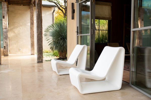 Image of an angled view of 2 all-weather Highcloud White Loop Lounge Chairs made with polyethylene in an outdoor setting. 