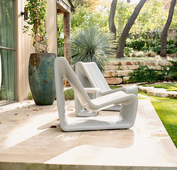 Image of a side view of 2 Highcloud White Loop Lounge Chairs made with polyethylene, displayed in an outdoor patio area.