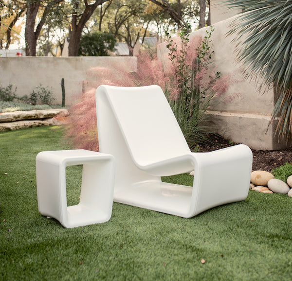 Image of a Highcloud White Loop Table beside the Highcloud white Loop Lounge chair displayed on outdoors on artificial turf. 