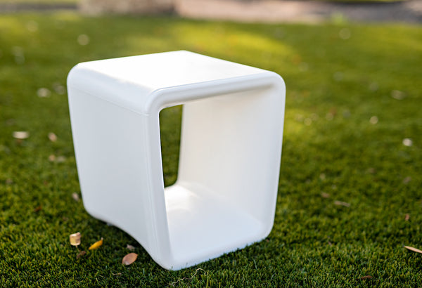Image of a sleek, UV-resistant Loop Table in the colour Highcloud White made with resin, sitting outdoors on artificial turf.